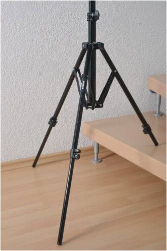 Een zwart statief staat op een houten vloer naast een trap. Het staat uitgeklapt en stevig.