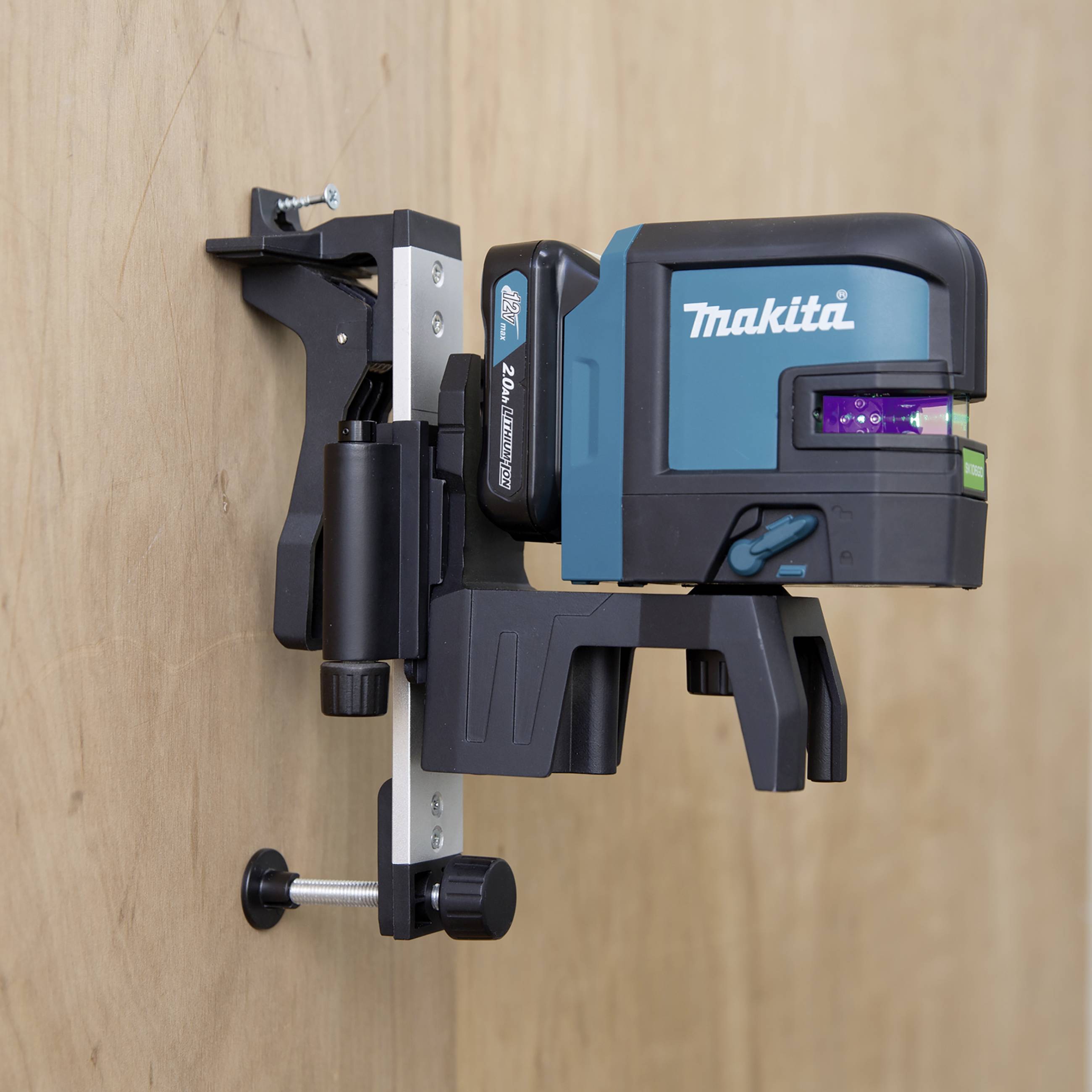 Een Makita laserwaterpas is aan een muur bevestigd. Het projecteert een groene laserstraal voor nauwkeurige uitlijning.