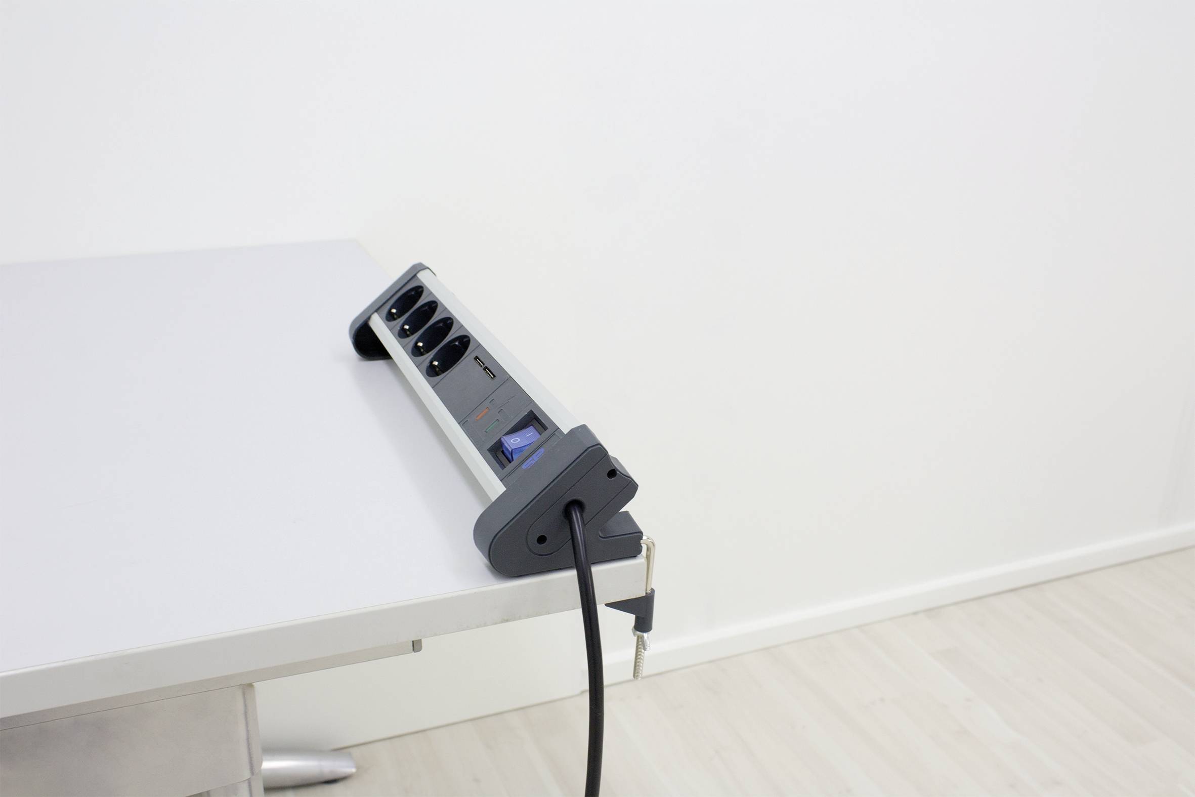 Een stekkerdoos met meerdere aansluitingen staat op tafel, gericht tegen de muur, met een aangesloten kabel.