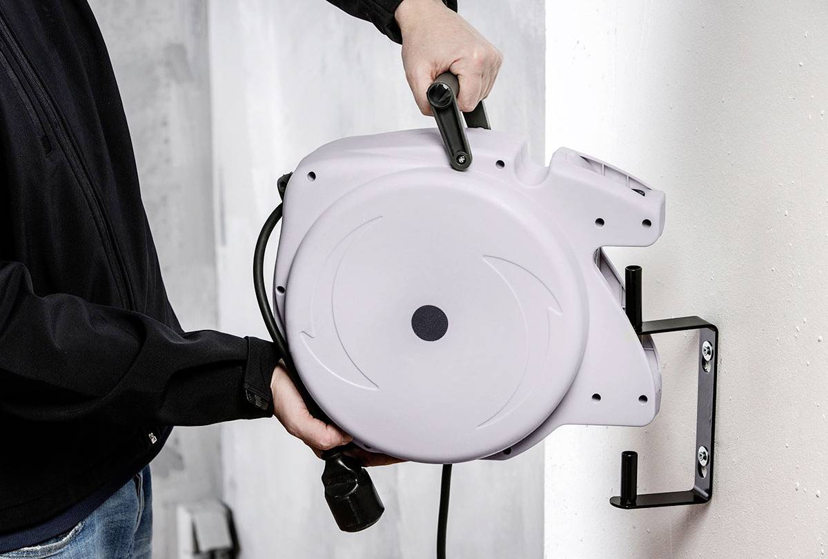 Een persoon bevestigt een grijze automatische kabeloproller aan een wandsteun.
