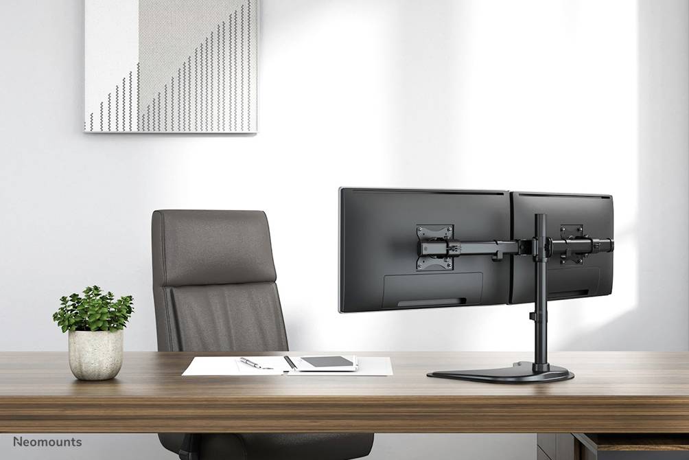 Een modern kantoor met een donker houten bureau, een lege lederen stoel, een dubbele monitorsteun voor twee monitoren en een kleine plantenpot.