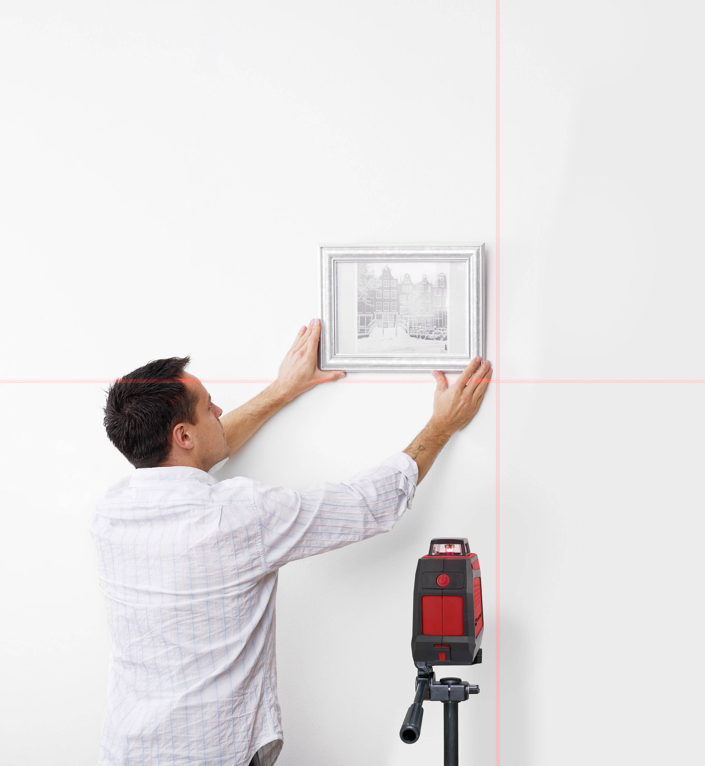 Een man hangt een schilderij aan de muur en gebruikt een laser voor nauwkeurige uitlijning, waarbij een rode lichtstraal de perfecte verticale en horizontale assen aangeeft.