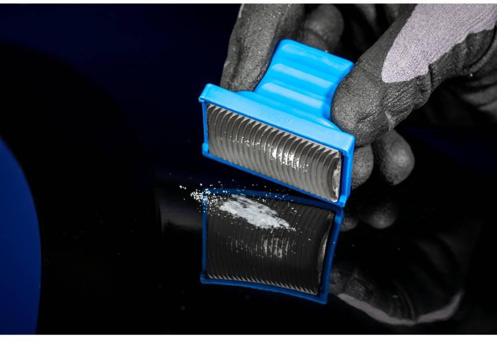 Een gehandschoende hand houdt een blauw apparaat vast om witte poederresten te verzamelen van een donker oppervlak.