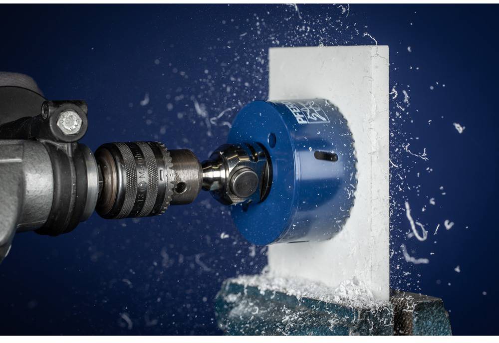 Boormachine met opzetstuk boort met hoge snelheid in een witte plaat; water spat eruit.