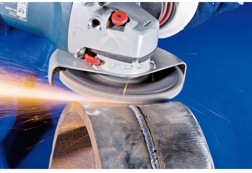 Een haakse slijper slijpt de lasnaad van een metalen buis. Vonken spatten rond terwijl het gereedschap het materiaal bewerkt.