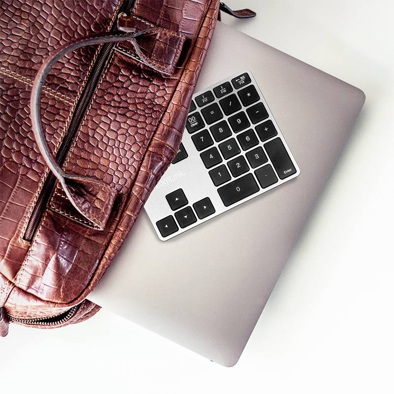 Een bruine leren rugzak ligt op een gesloten zilveren laptop, waarop een extern toetsenbord is geplaatst.