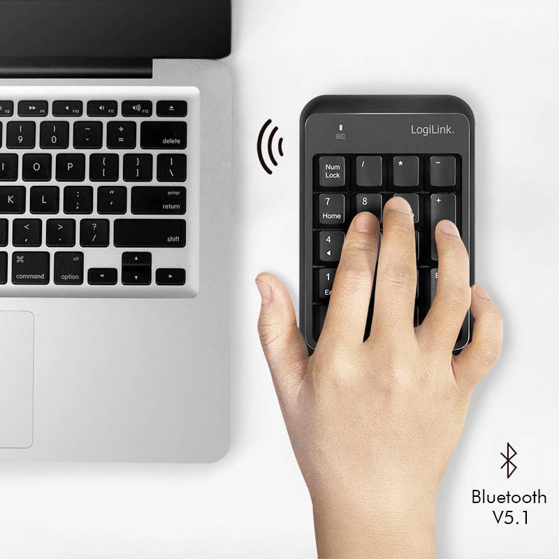 Een hand gebruikt een draadloos numeriek toetsenbord naast een laptop. Het numerieke toetsenbord verbindt zich via Bluetooth, versie 5.1.