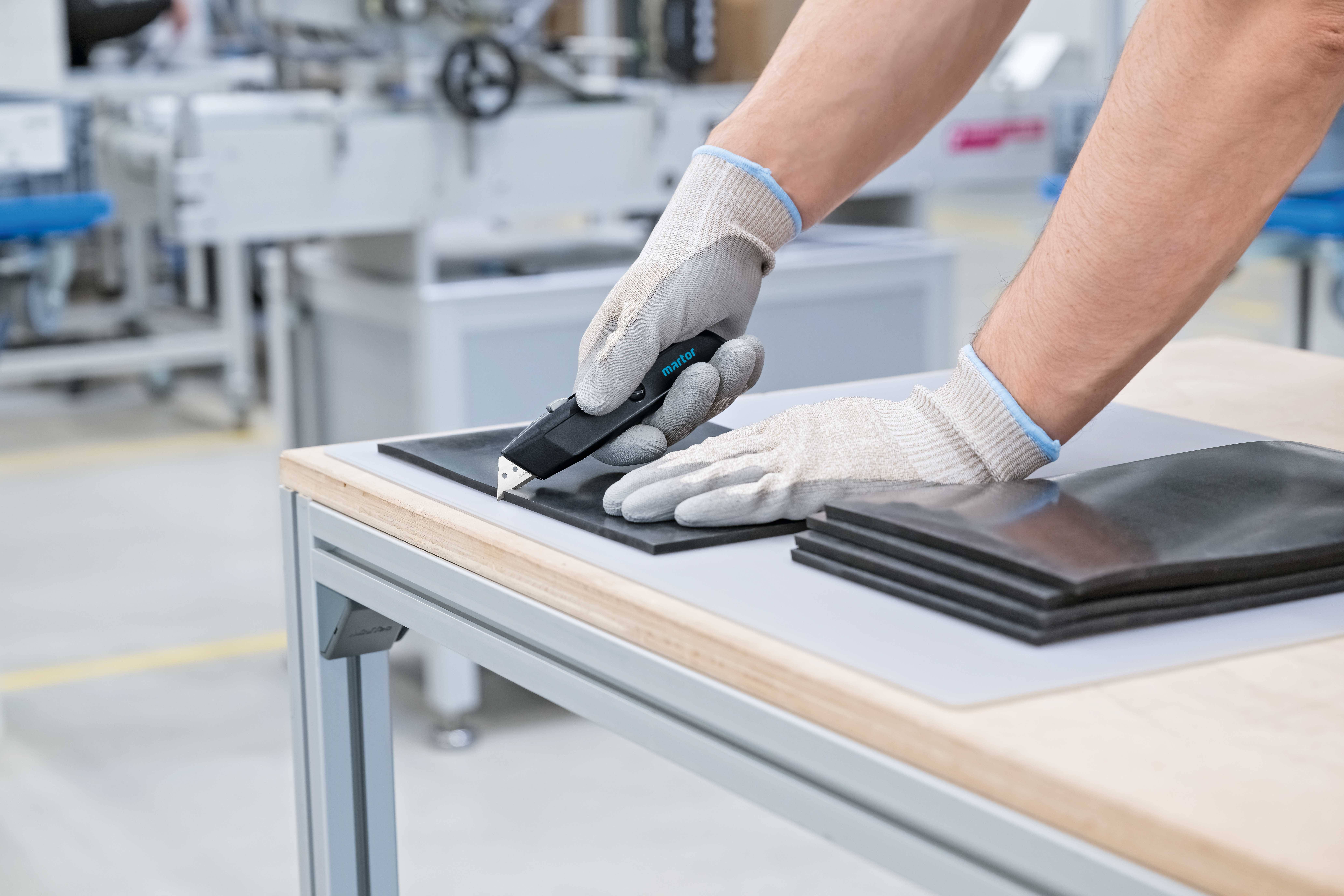 Een persoon met handschoenen snijdt dunne materialen met een precisegereedschap op een tafel in een werkplaats.