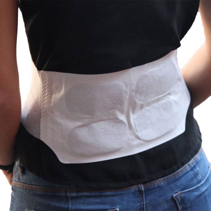 Een persoon draagt een witte rugverwarmer of warmtekussen onder een zwart T-shirt dat om de taille is vastgemaakt.