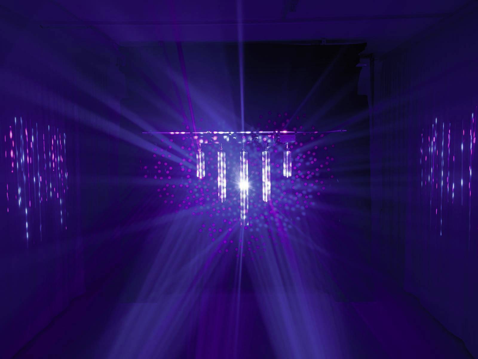 Een ruimte met donkerblauwe verlichting, waarin heldere, gekleurde lichtstralen vanuit een centraal punt uitstralen en de ruimte verlichten.