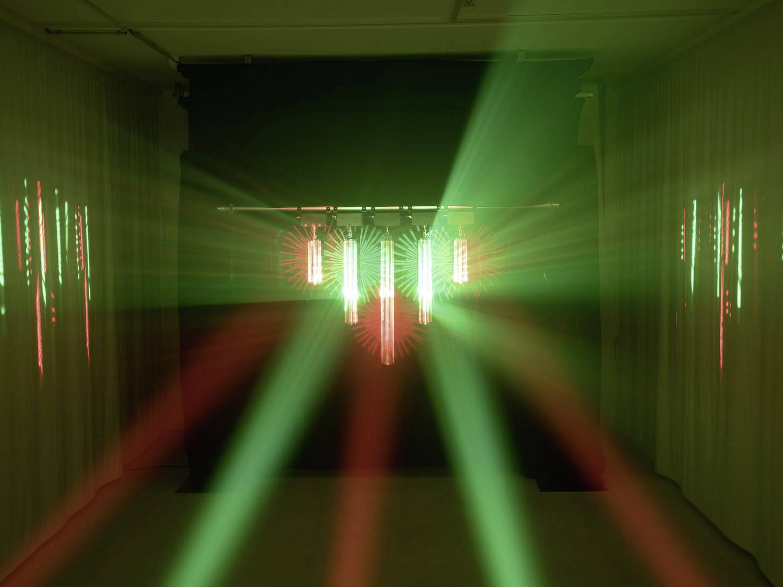 Lichtinstallatie in een donkere ruimte met rode en groene stralen die uitgaan van meerdere verticale lichtbronnen.