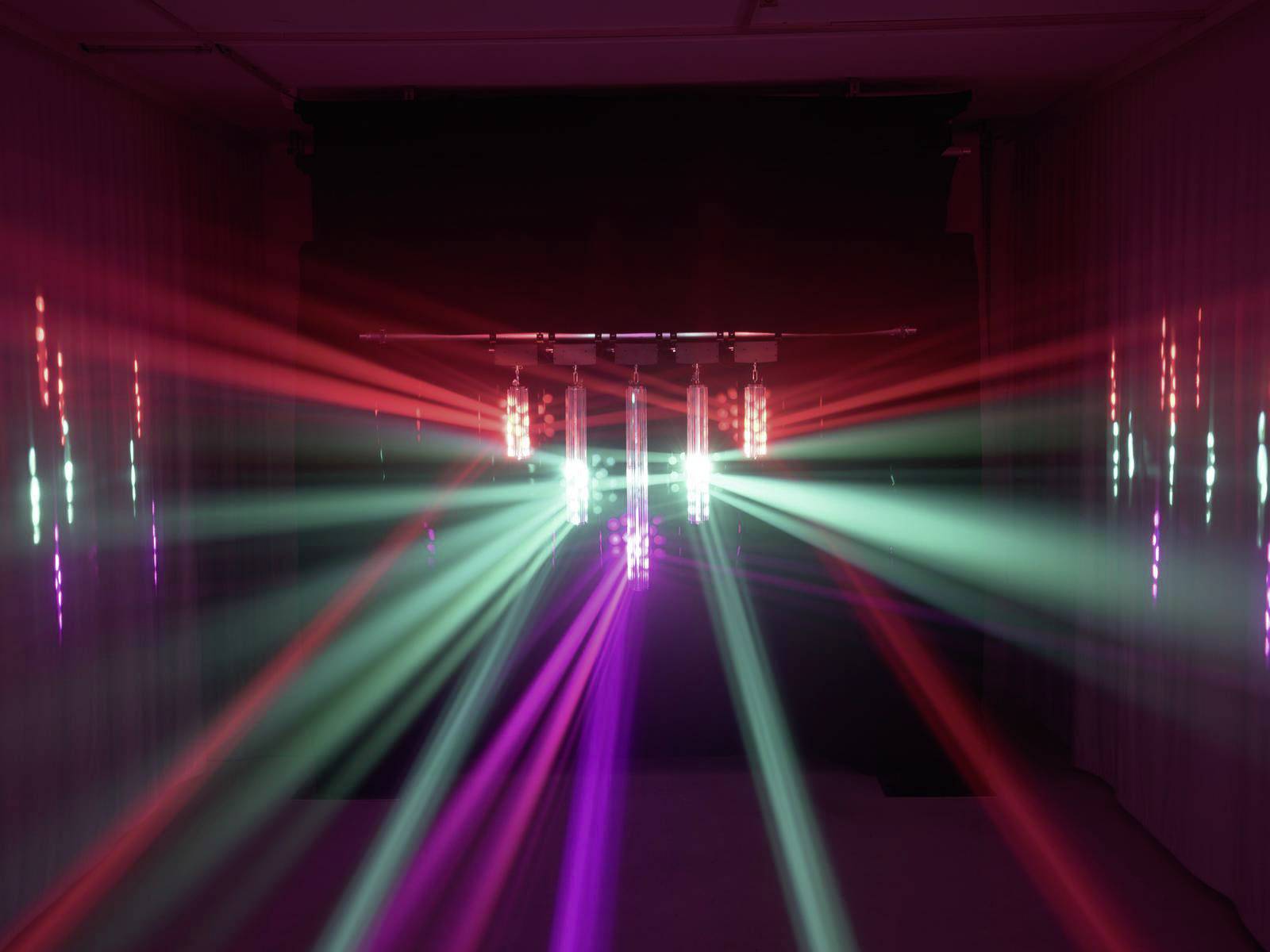 Kleurrijke lichten stralen uit in een donkere ruimte, met rode, groene en paarse laserbundels die kruiselings door elkaar heen bewegen.