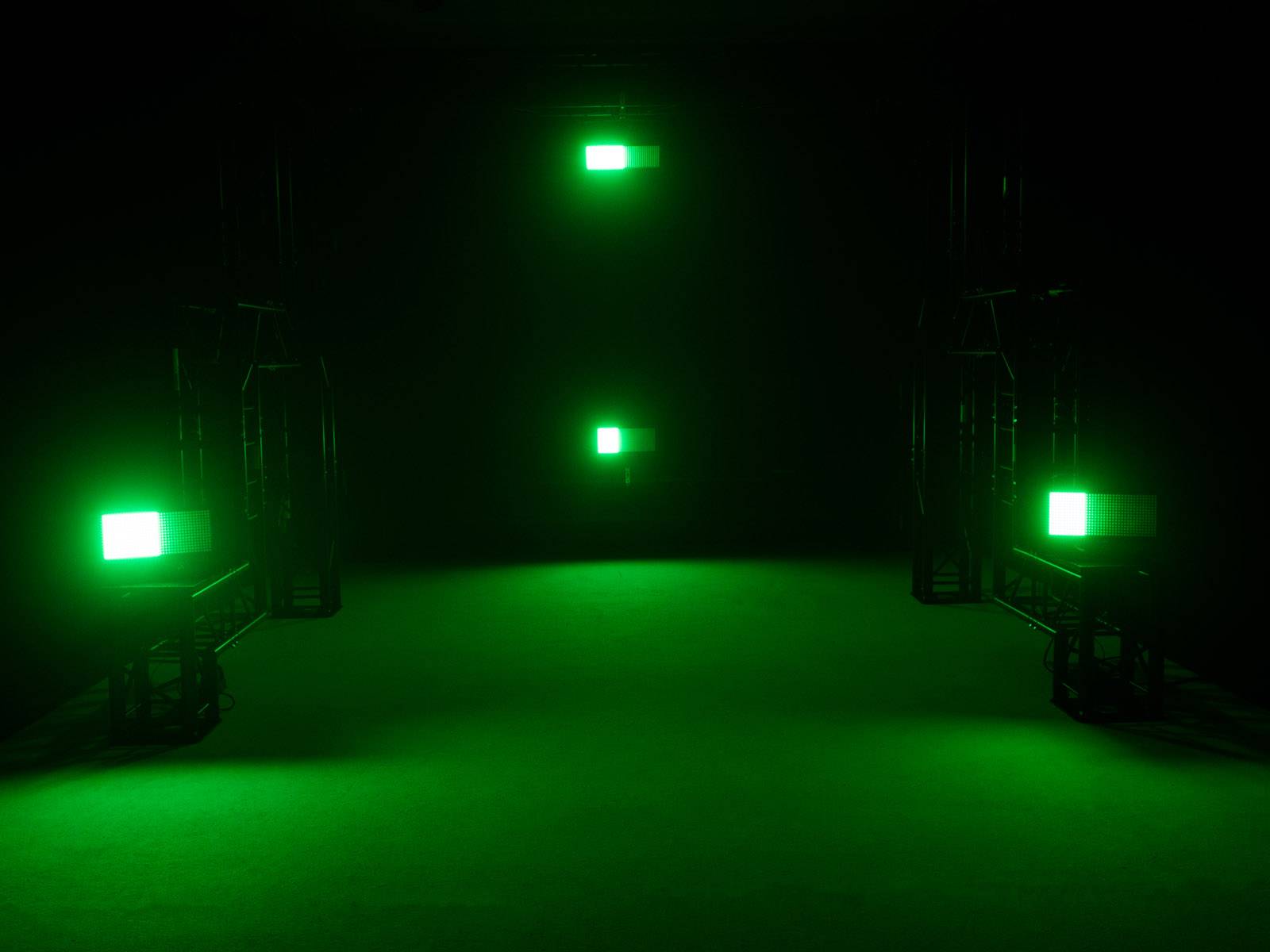 Een donkere ruimte met vier lichtgevende groene vierkanten, symmetrisch gerangschikt aan de muren en de vloer, verlicht de scène.