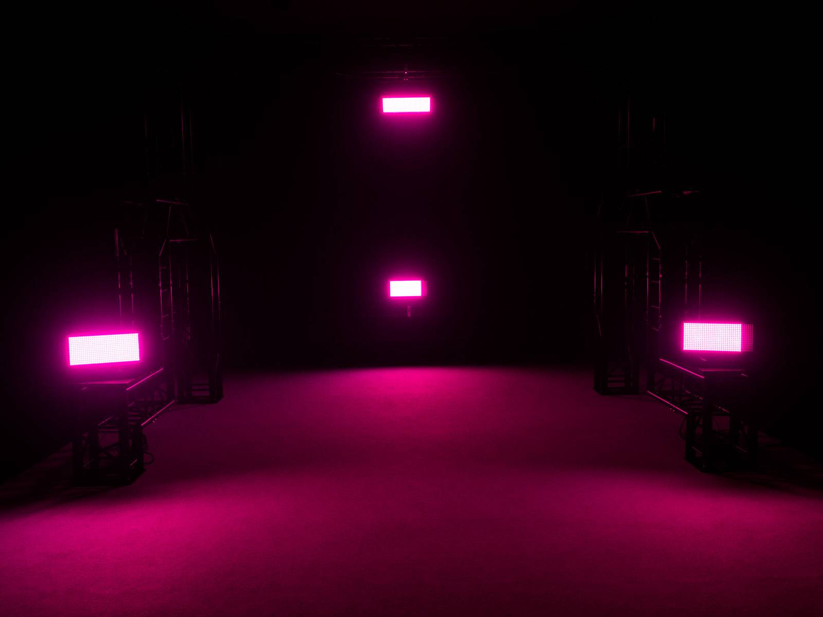 Donkere ruimte met drie rechthoekige, lichtgevende roze lichten aan de muren en vloeren die een futuristische sfeer creëren.