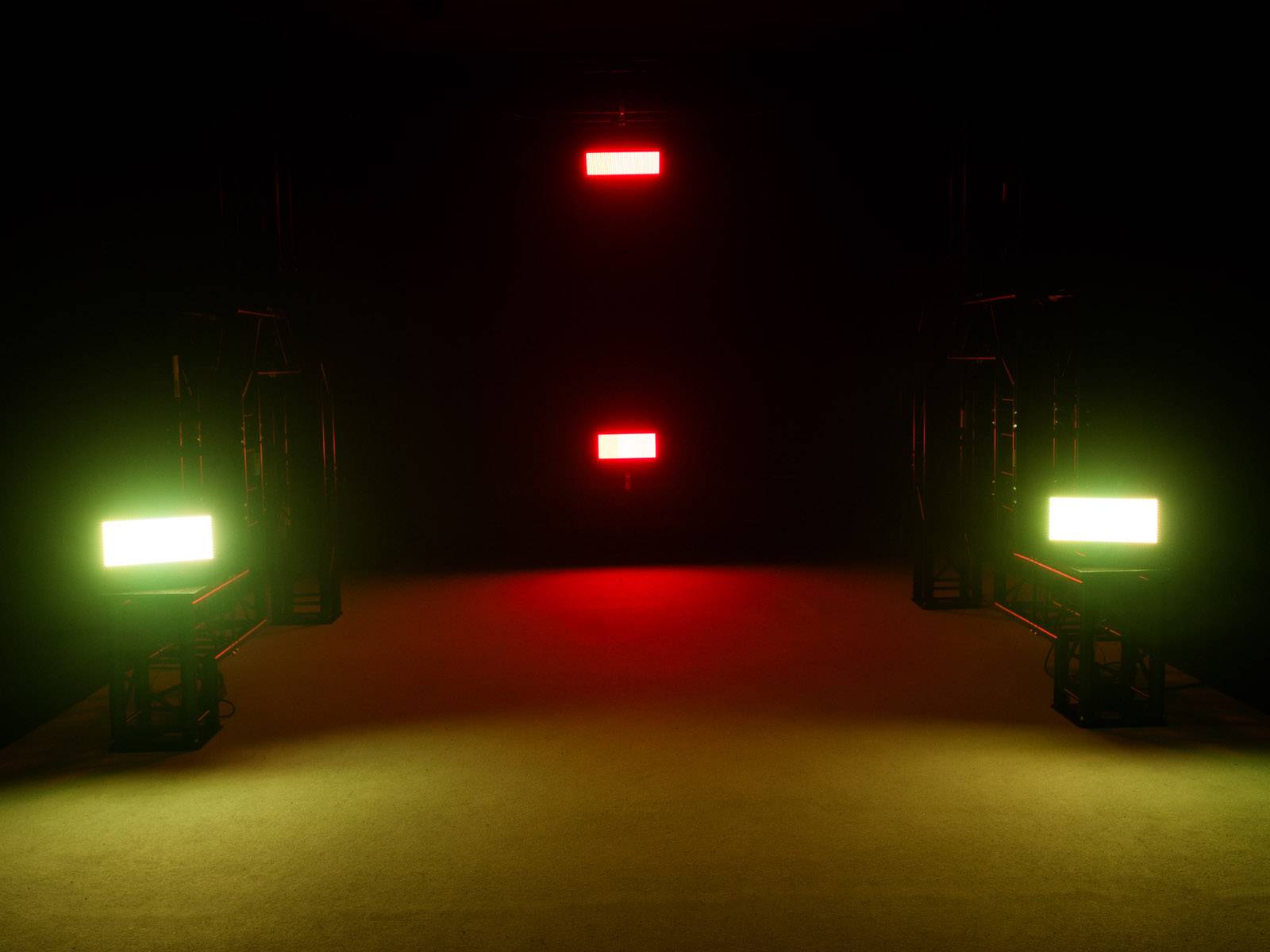 Een donkere ruimte met drie rechthoekige lichten: twee groene lichten onderaan links en rechts, een rood licht bovenaan in het midden.