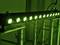 Acht groene lampen op statief, verlicht door een lichtband, tegen een donkere achtergrond.