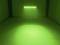 Een ruimte met groen licht dat van bovenaf op een gestructureerd oppervlak schijnt. Op de achtergrond is een metalen frame zichtbaar.