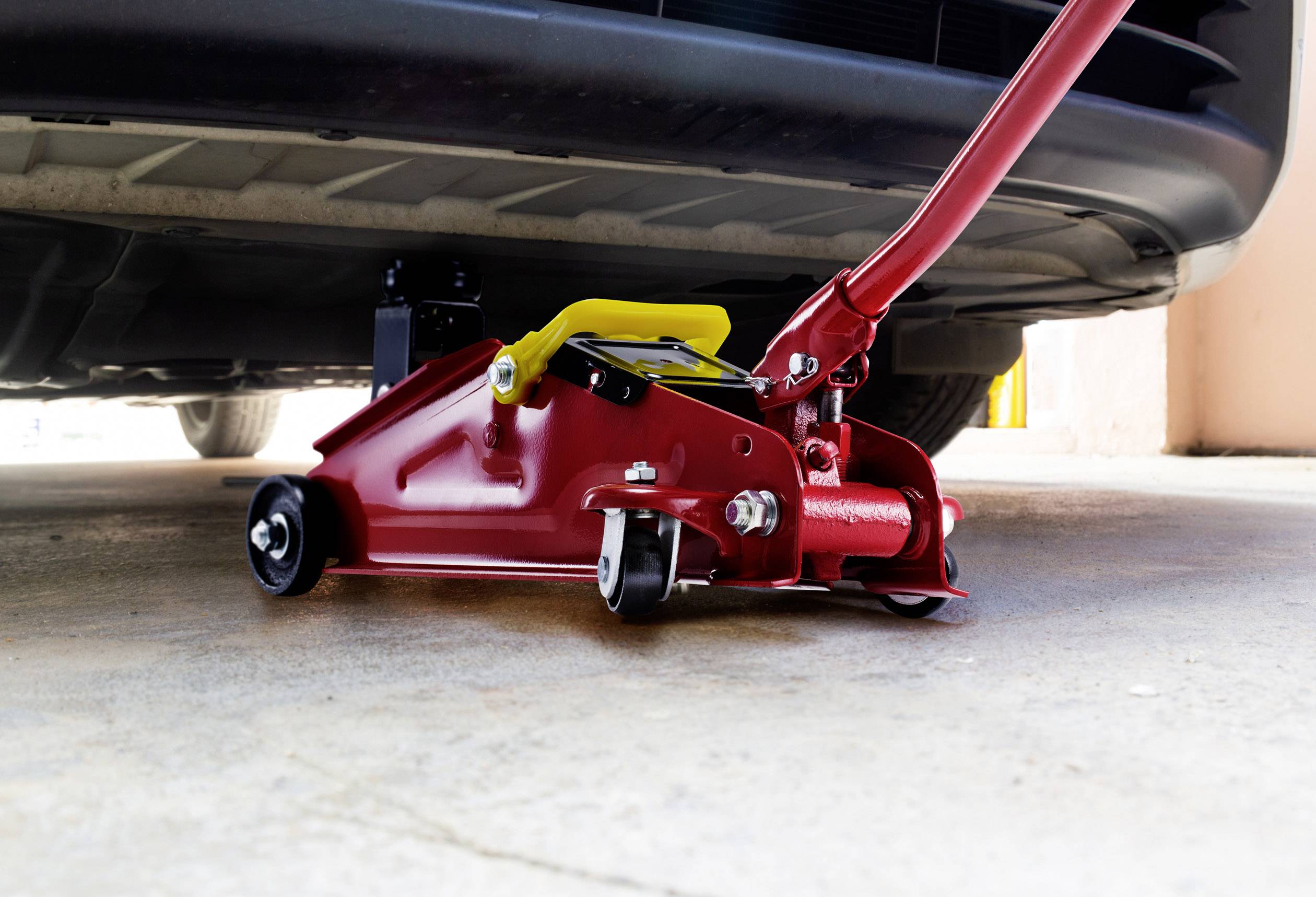 Een rode krik tilt een auto op in een garage. De krik bevindt zich onder het voorste deel van het voertuig.