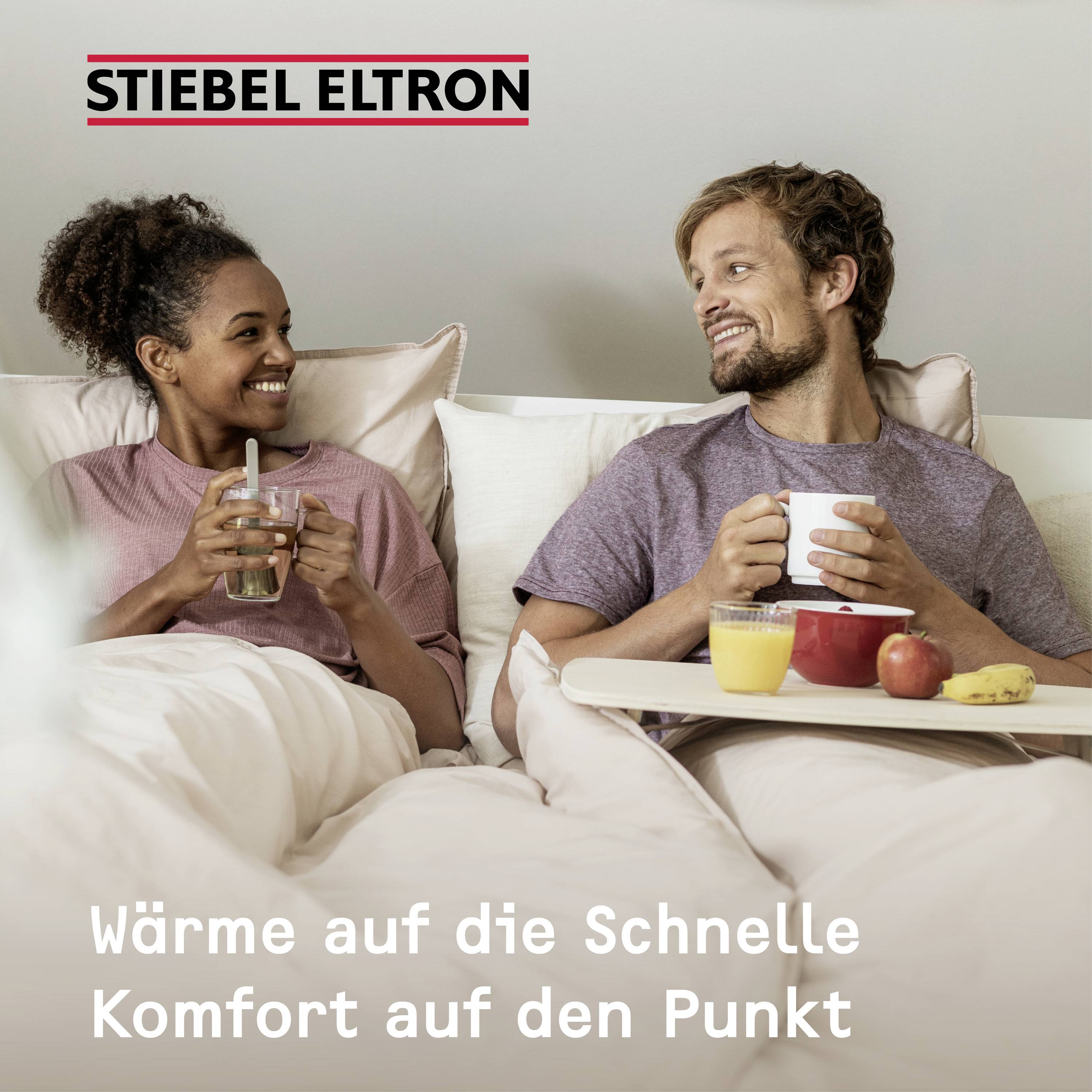 Een lachend stel zit op een bank, geniet van ontbijt met koffie en fruit. Linksboven het logo 'Stiebel Eltron'. Tekst onderaan: 'Snel warmte, comfort tot in de puntjes'.