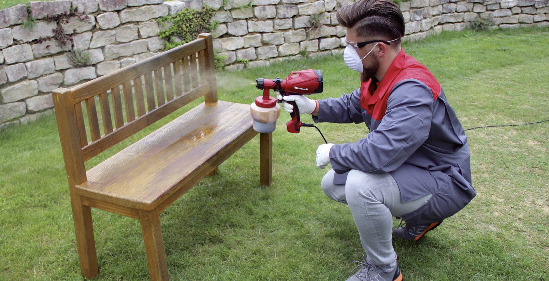 Persoon in beschermend pak desinfecteert een deur in een gebouw met een sproeapparaat. Bord zegt: 'Ook geschikt voor oppervlaktedesinfectie met spray'.