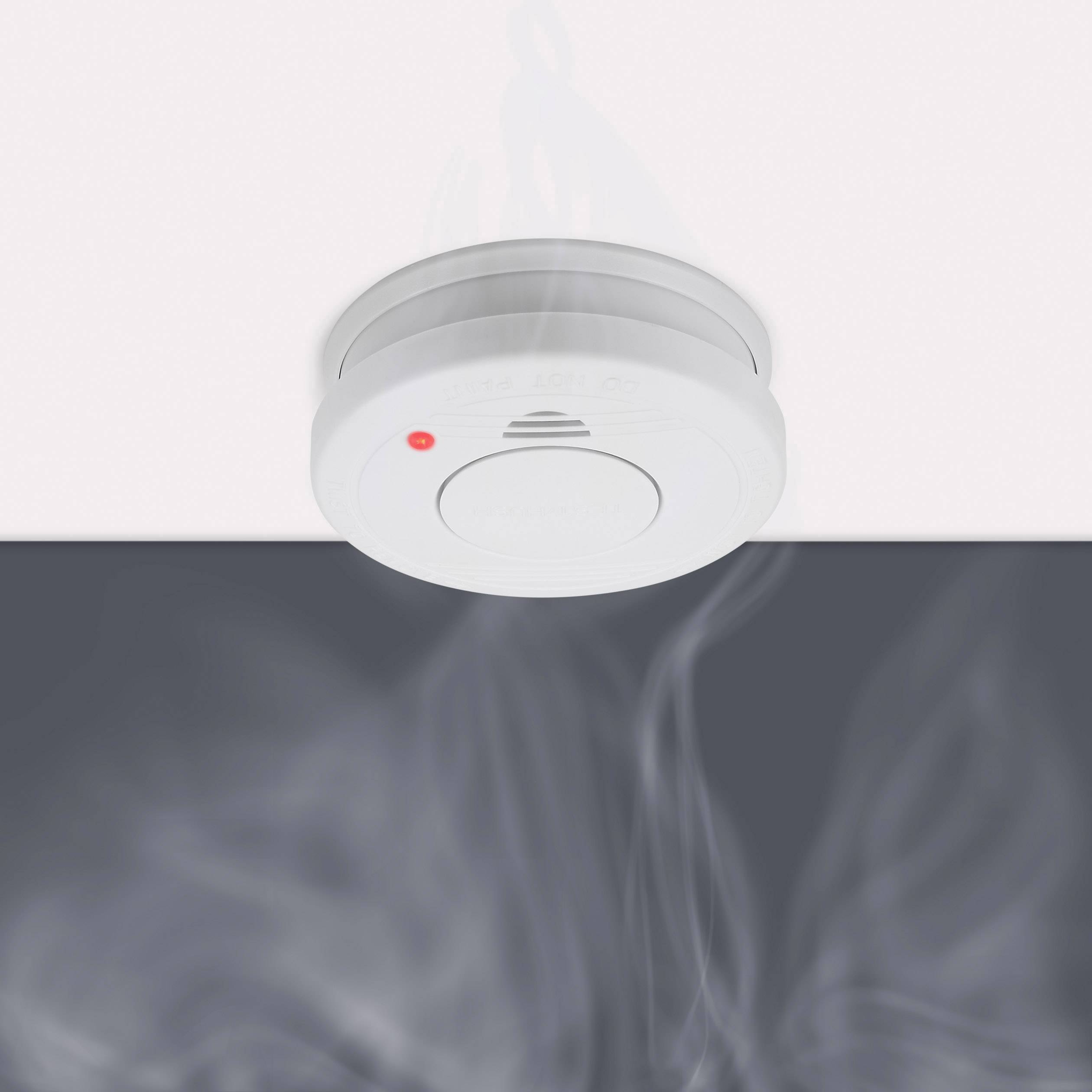Een rookmelder aan het plafond met opkomende rook eronder. Een rode LED brandt, wat wijst op een alarm.