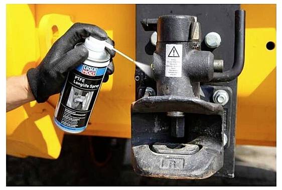 'Een persoon die een zwarte handschoen draagt, brengt PTFE-langdurige spray aan op het koppelingsbereik van de machine, wat de smering verbetert en de wrijving vermindert.'