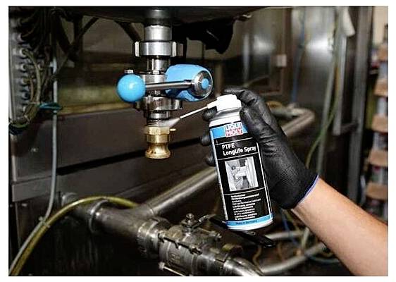 Persoon in handschoen spuit smeermiddel op een metalen kraan, mogelijk voor onderhoud.