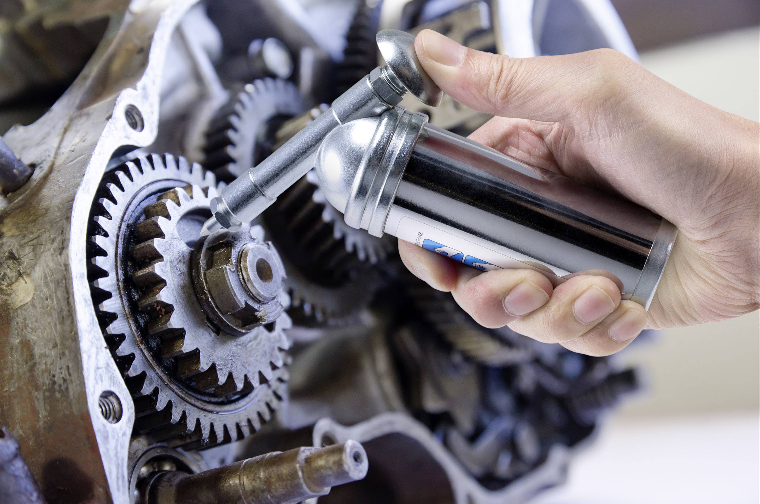 Een hand smeert de tandwielen van een mechanisch apparaat met een oliekan.