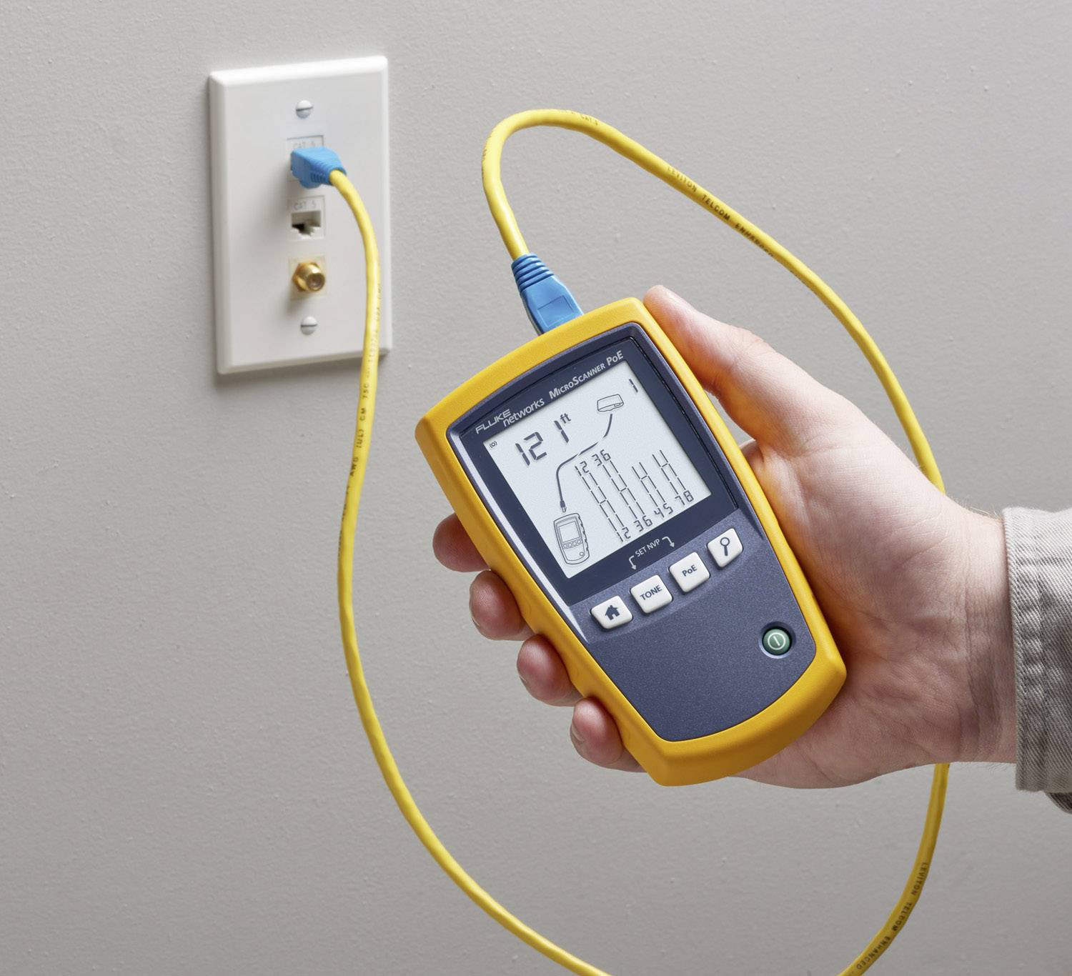 Een hand houdt een geel kabeltest-apparaat vast dat is aangesloten op een netwerkaansluiting om de kabelverbinding te controleren.