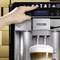 Een hand bedient een Siemens-koffiemachine om een cappuccino te maken. Een kopje cappuccino staat onder de uitloop.