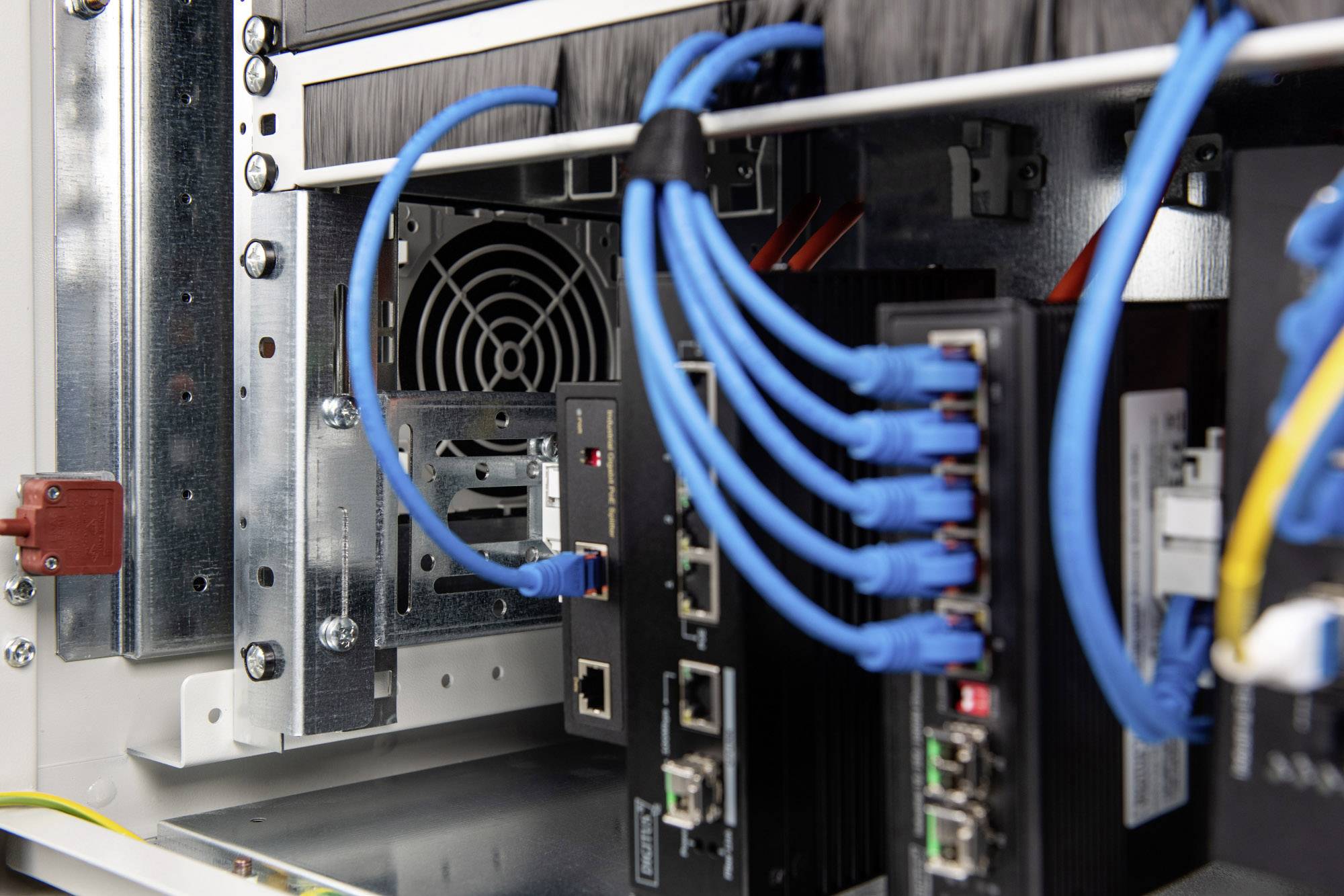 Serverruimte met meerdere aangesloten netwerkkabels en hardwarecomponenten. Ventilator zichtbaar op de achtergrond.