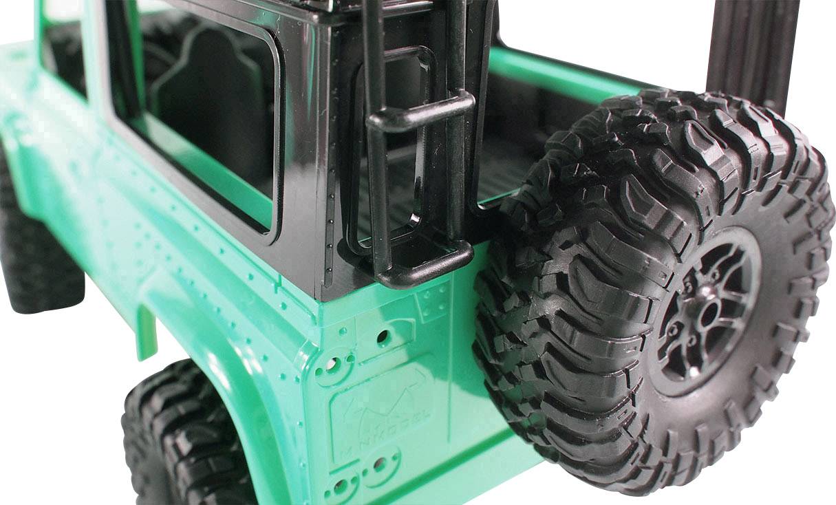 Een modelauto met een groen chassis en grote, gedetailleerde banden is te zien. De auto heeft open vensterframes en een ladder aan de zijkant.