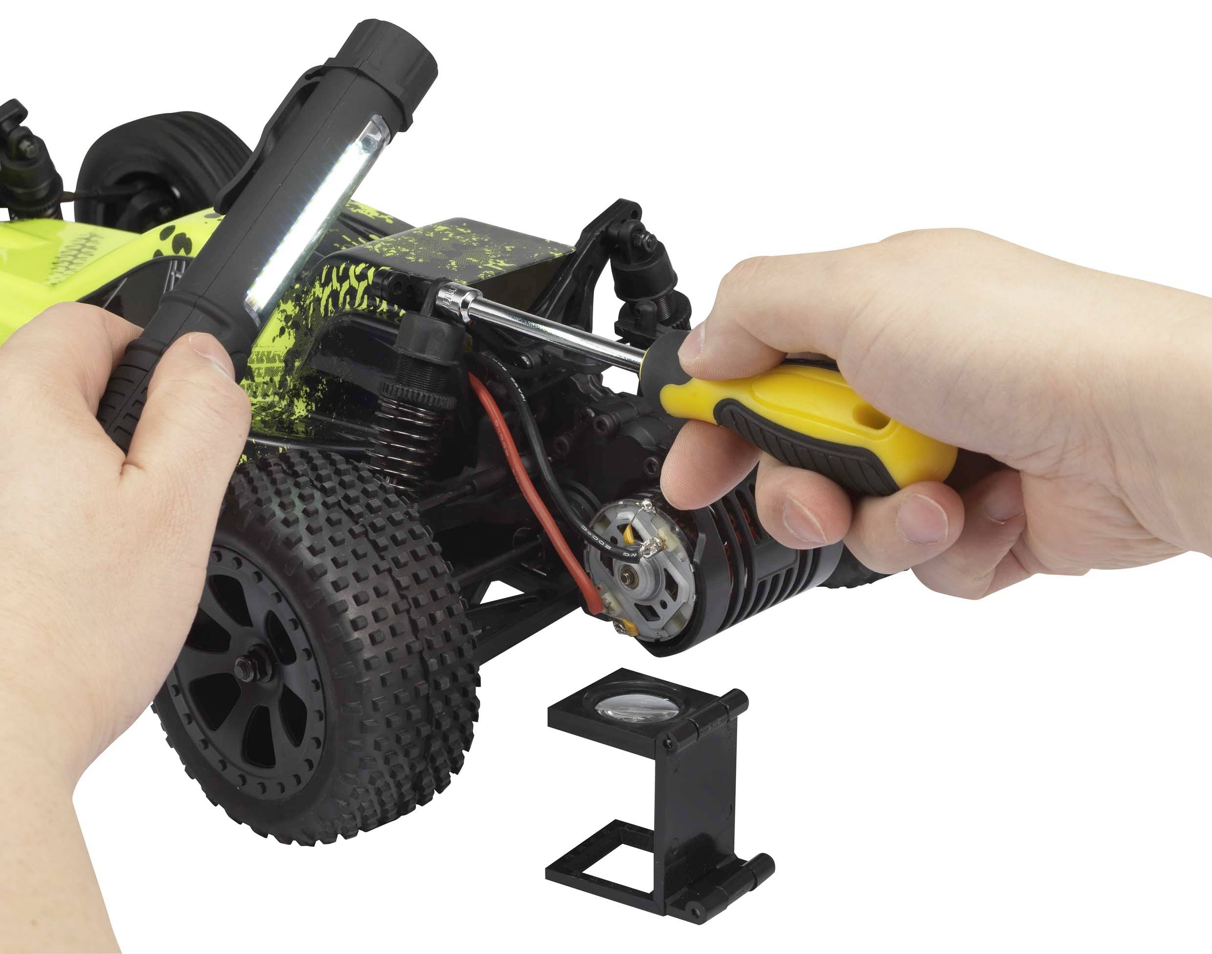 Een persoon schroeft met een schroevendraaier aan een bestuurbare auto. Een lamp verlicht de werkruimte.