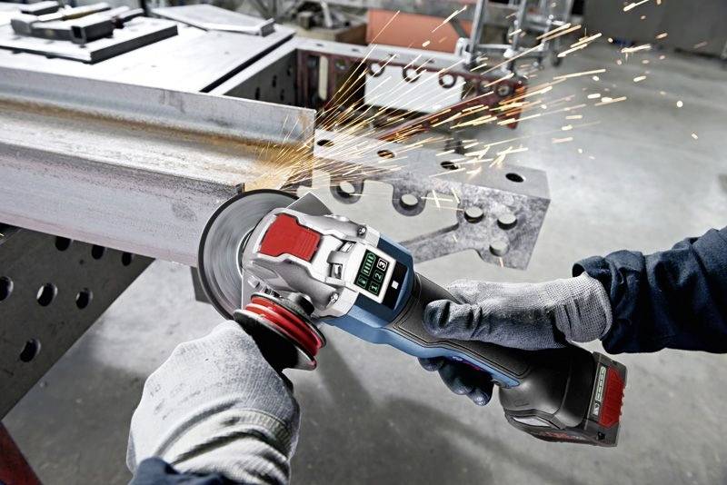 Een ambachtsman slijpt metaal met een haakse slijper. Vonken spatten rond. De werkplek is industrieel en functioneel ingericht.