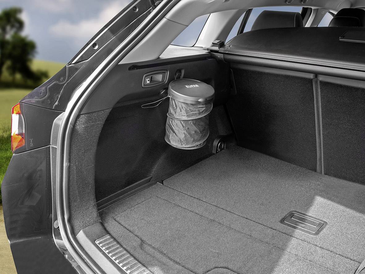 'Een lege kofferbak van een auto met een opvouwbare prullenbak bevestigd aan de zijwand, naast een graslandschap op de achtergrond.'