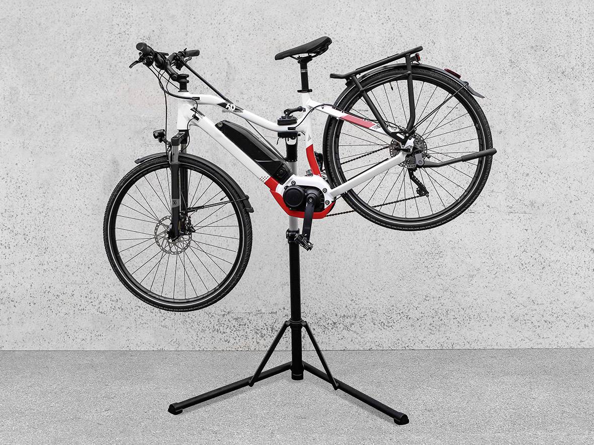 Een wit-zwarte fiets is bevestigd op een zwarte reparatiestandaard, naast een grijze muur.