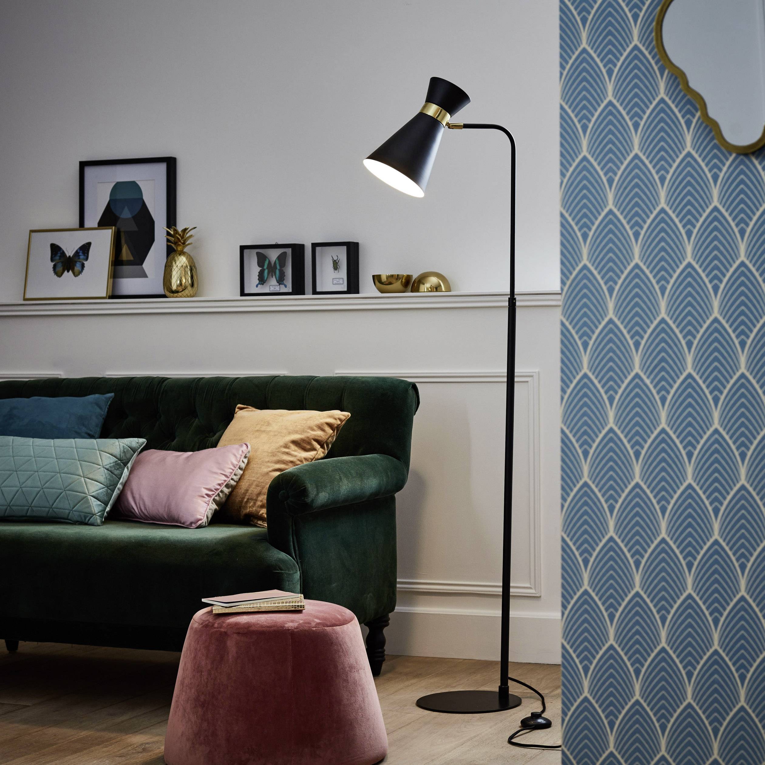 Een stijlvol ingericht woonkamer met een donkergroen bankstel, pastelkleurige kussens, een staande lamp en fotolijsten op een plank.