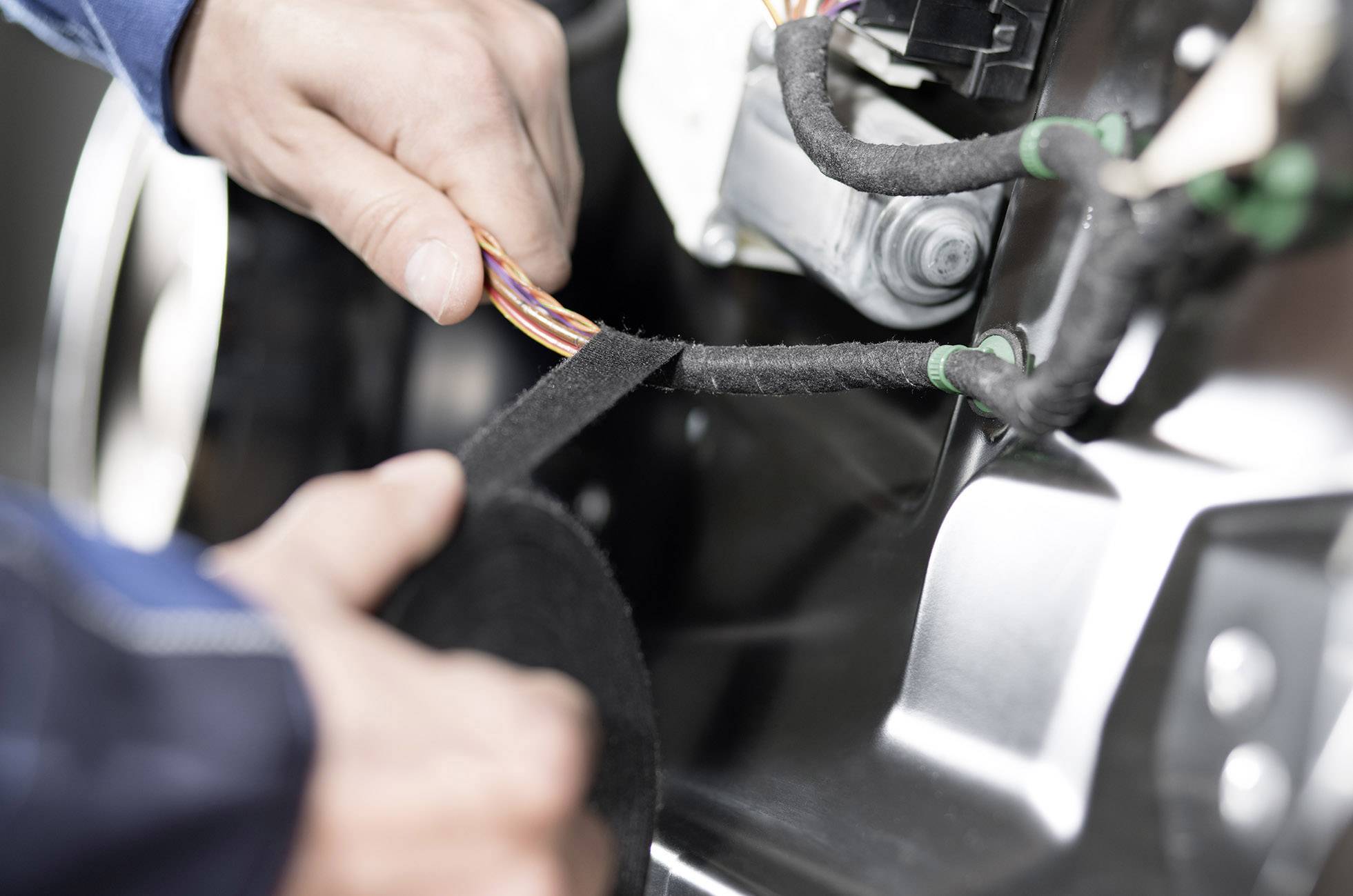 Een persoon wikkelt isolatietape om een kabel bundel in een machine of apparaat. Handen werken dicht bij technische componenten.
