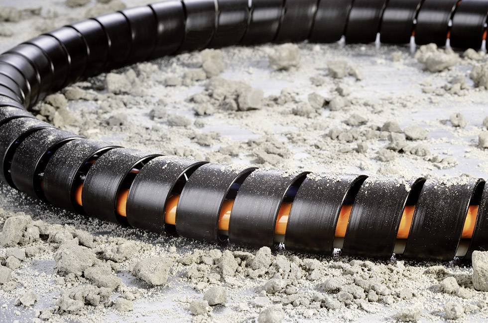 Een zwart, spiraalvormig kabel bedekt met zand op een oppervlak. Het kabel heeft oranje secties aan de binnenkant.