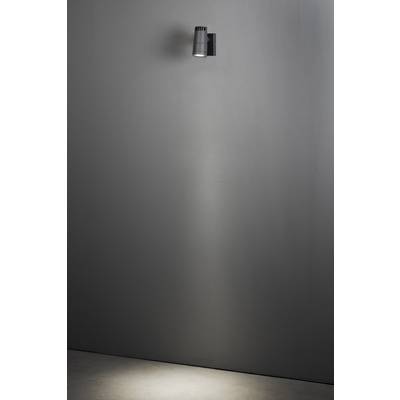 Een enkele wandlamp verlicht een gedeelte van een verder kale grijze muur, waardoor een heldere lichtkegel ontstaat.