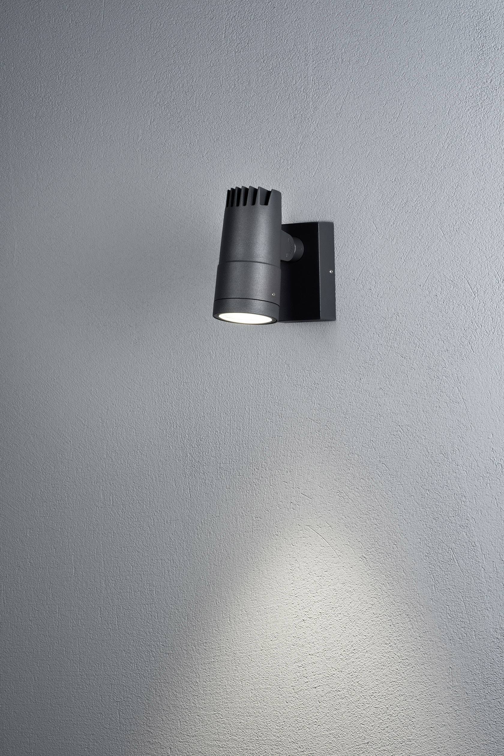 Een zwarte wandlamp verlicht de grijze muur met een krachtige lichtstraal naar beneden.