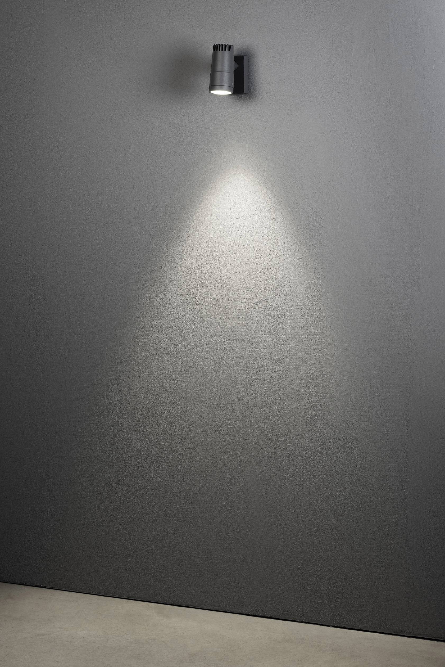 Een grijze muur met een plafondgemonteerde spotlamp die een helder lichtkegel op de muur werpt.