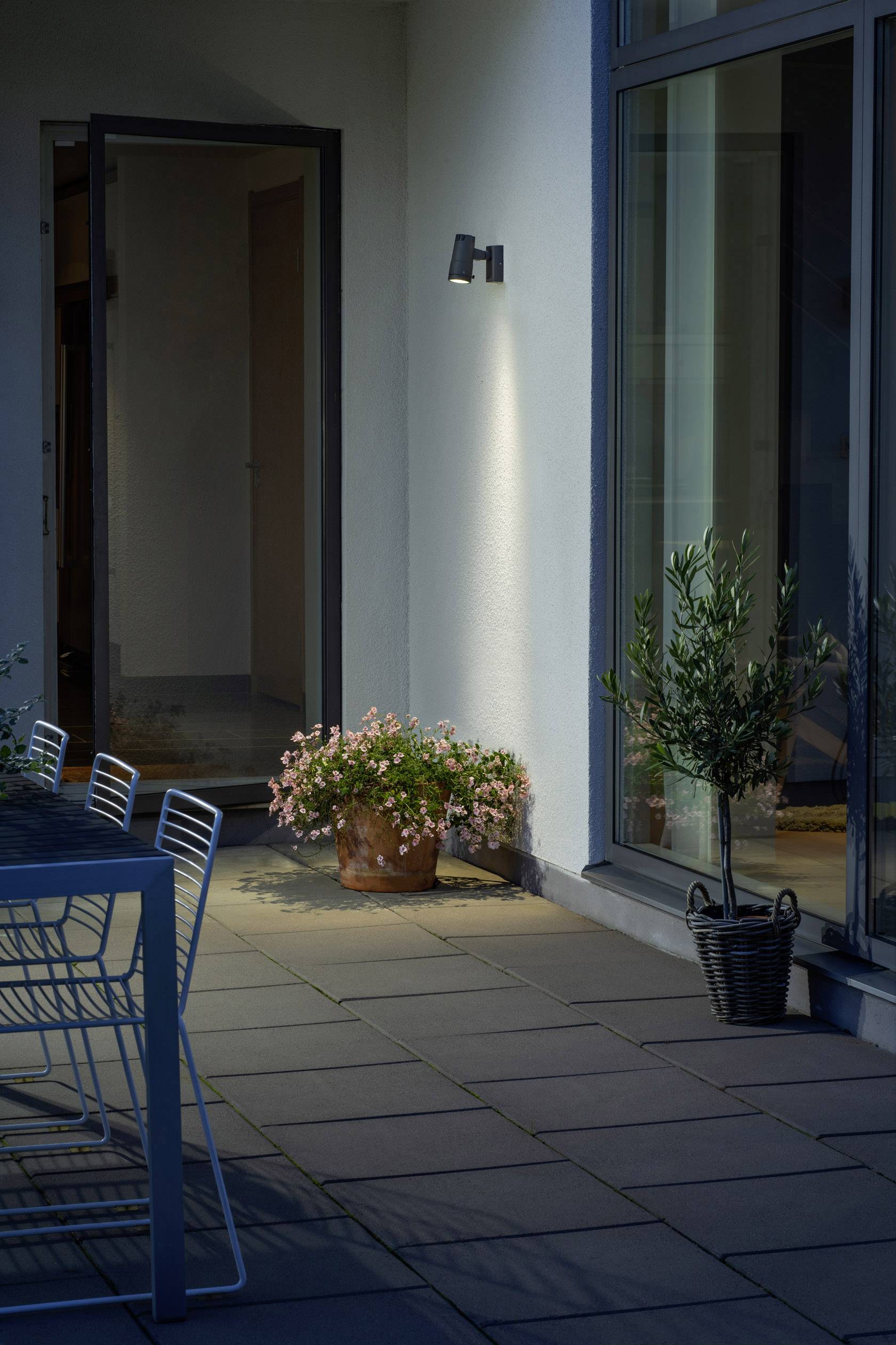 Een open terrastoegang bij schemering, met bloeiende planten en moderne metalen stoelen. Een aangename avondsfeer.