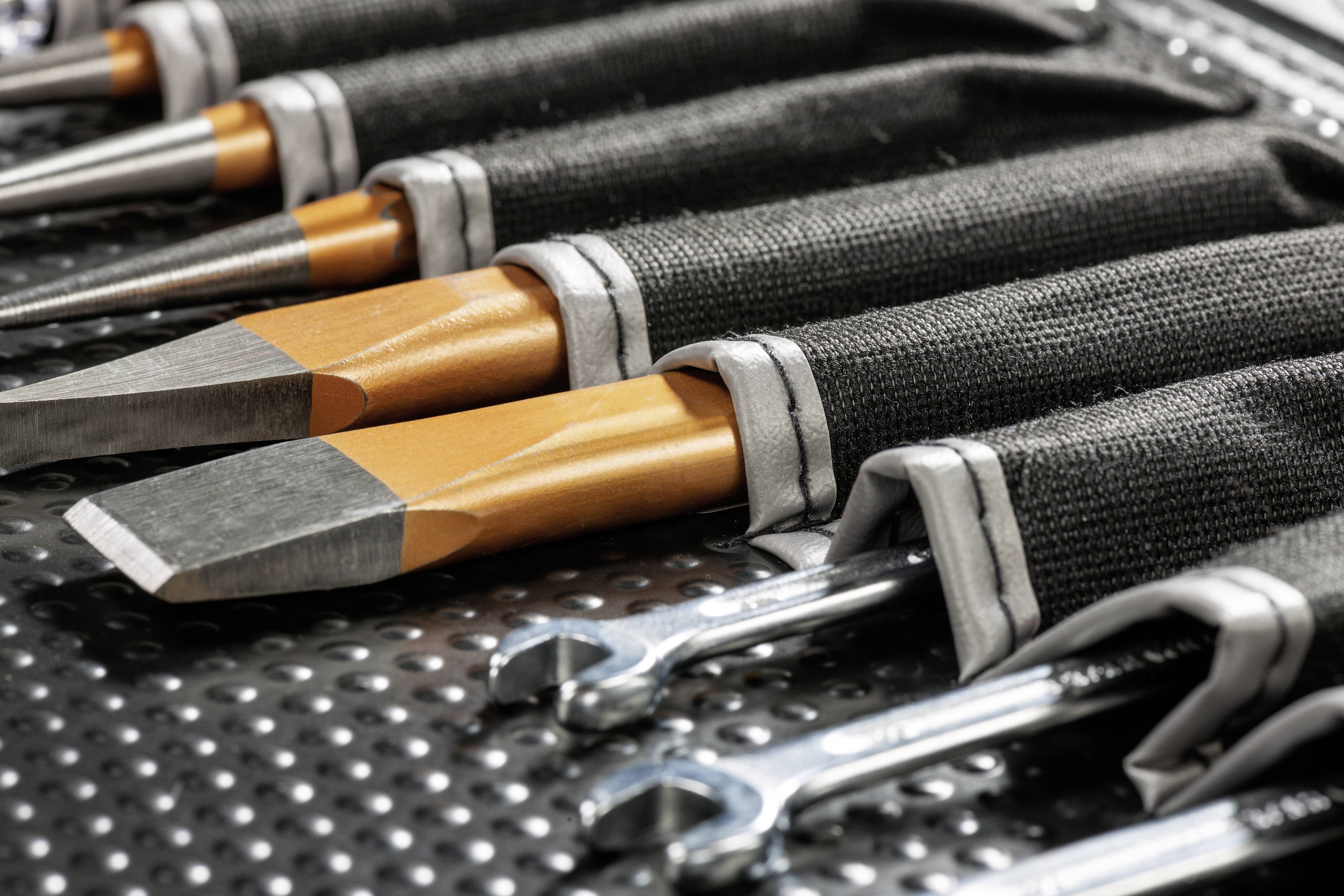 Een reeks gereedschappen, waaronder metalen beitels en moersleutels, zorgvuldig gerangschikt in een zwarte gereedschapstas.