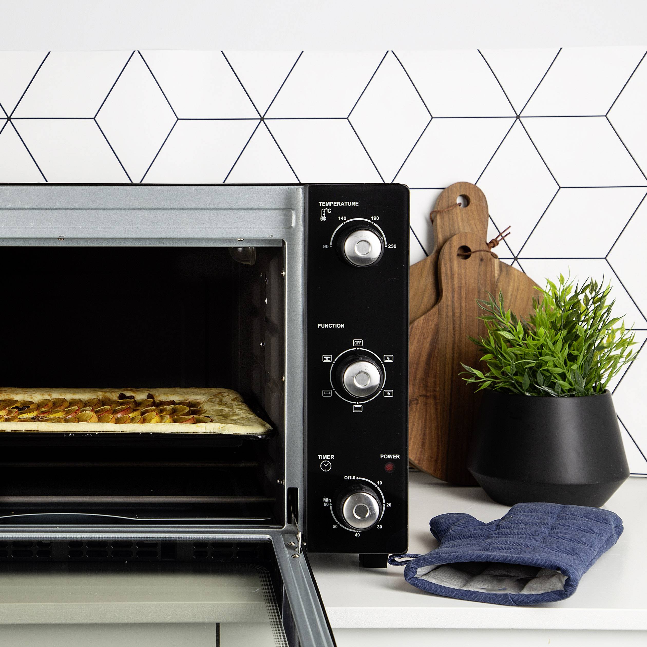 Een oven met een openstaande deur toont een bakplaat met gebakken koekjes. Ernaast bevinden zich een snijplank en een plant.