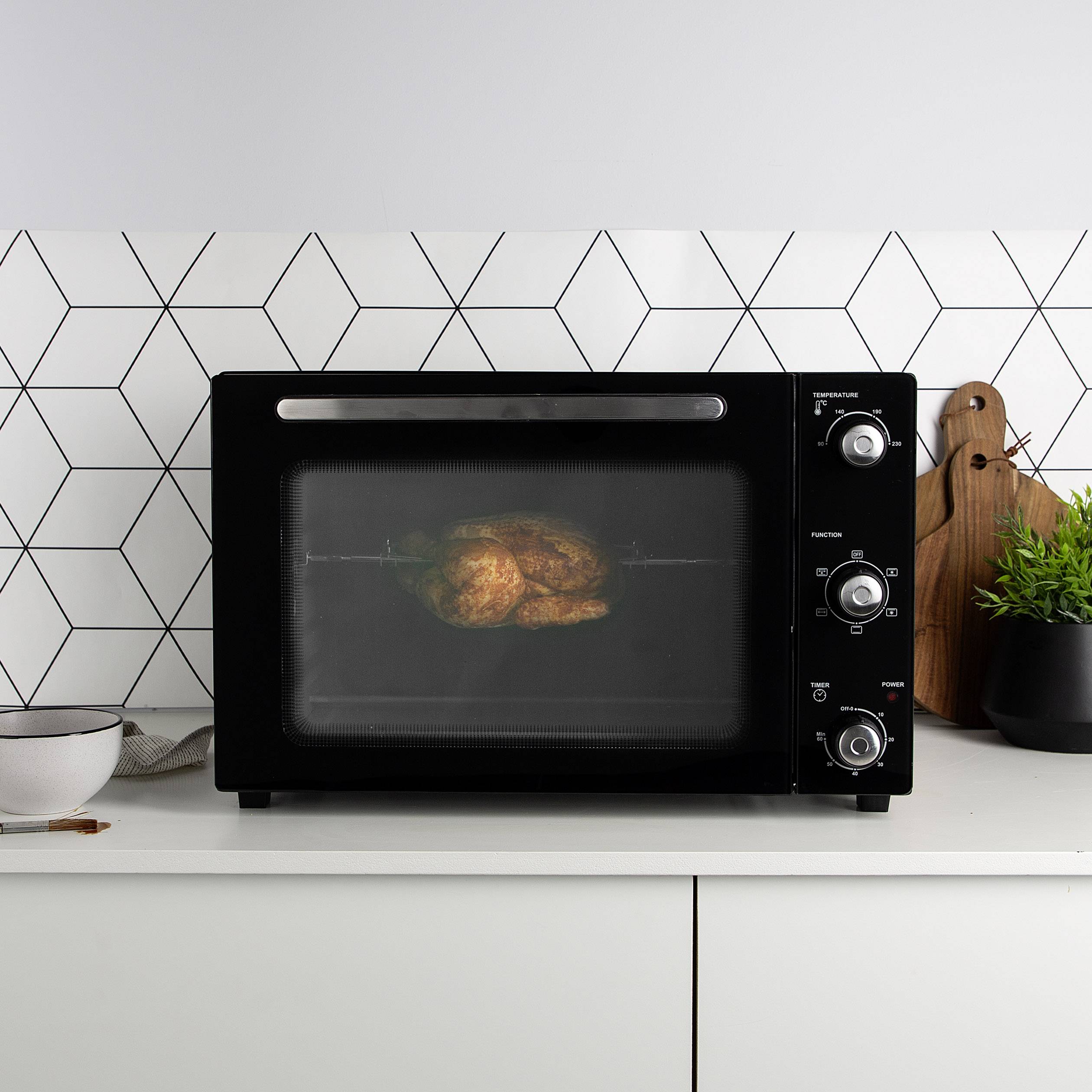 Een zwarte oven op een wit aanrecht. Een braadkip wordt aan het bereiden binnenin.