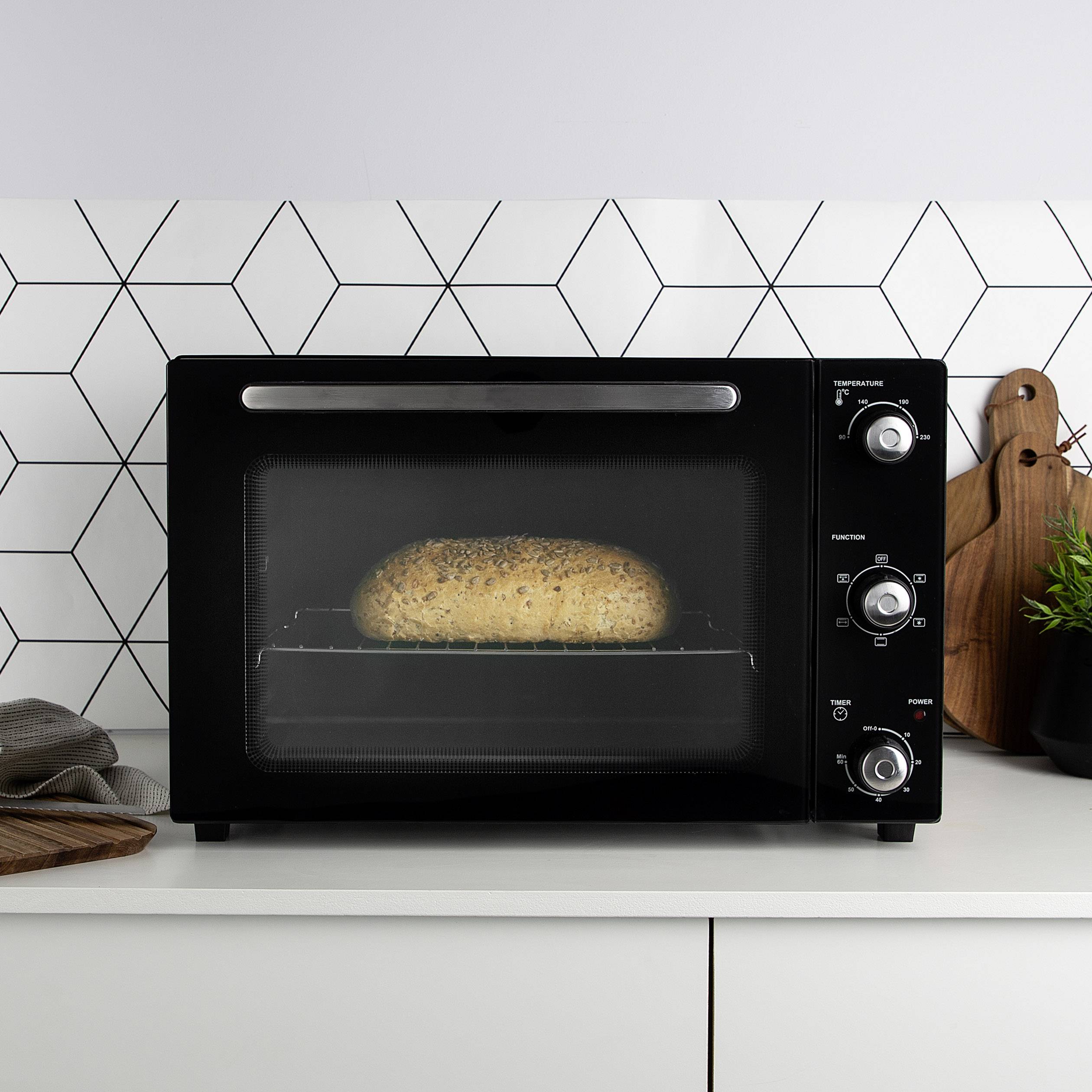 Een oven op een werkblad, waar een brood in wordt gebakken. Op de achtergrond is een geometrische wanddecoratie te zien.