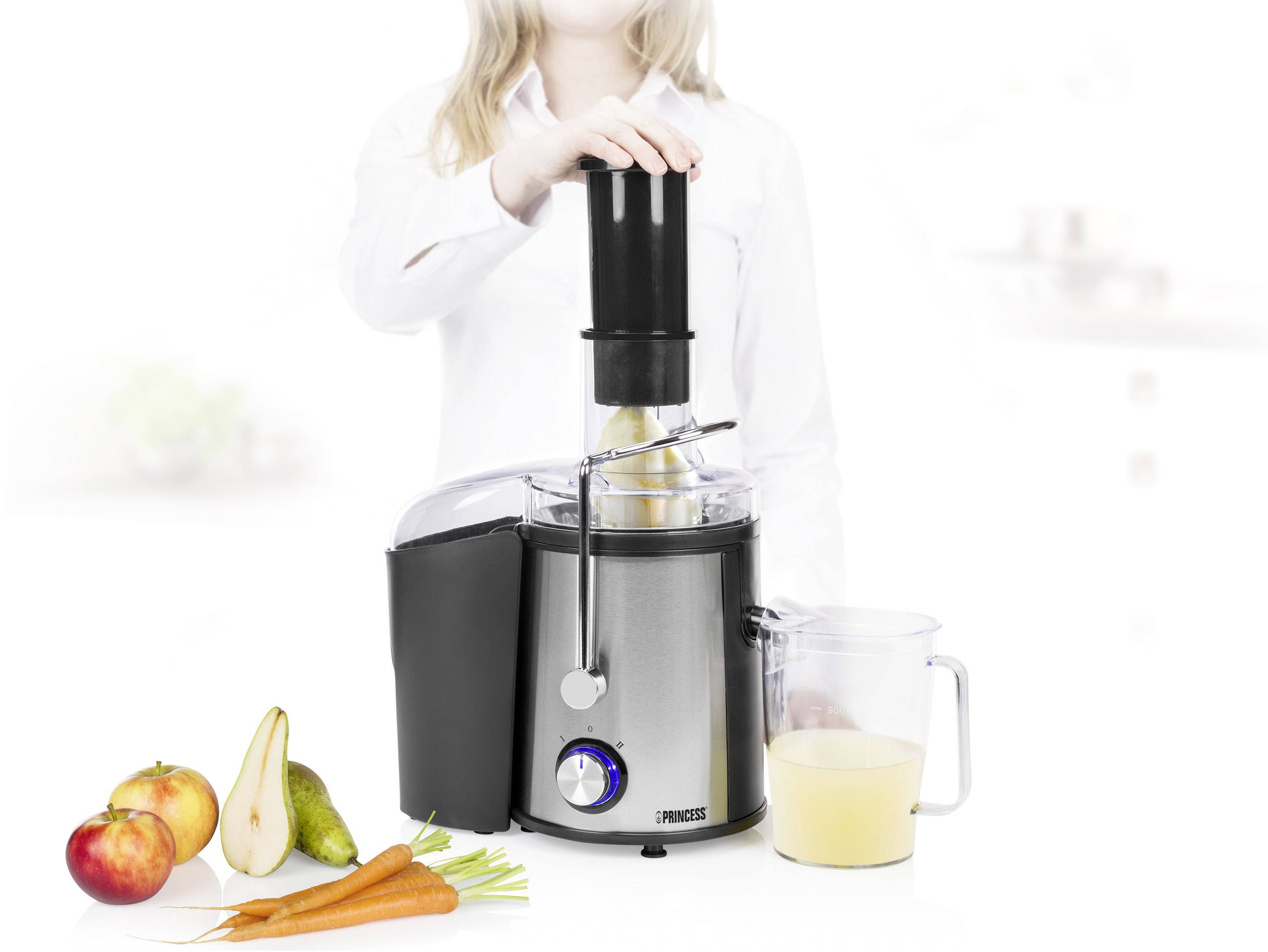 Vrouw bedient sapcentrifuge met fruit en groenten ernaast. Verse sap wordt verzameld in een kan.