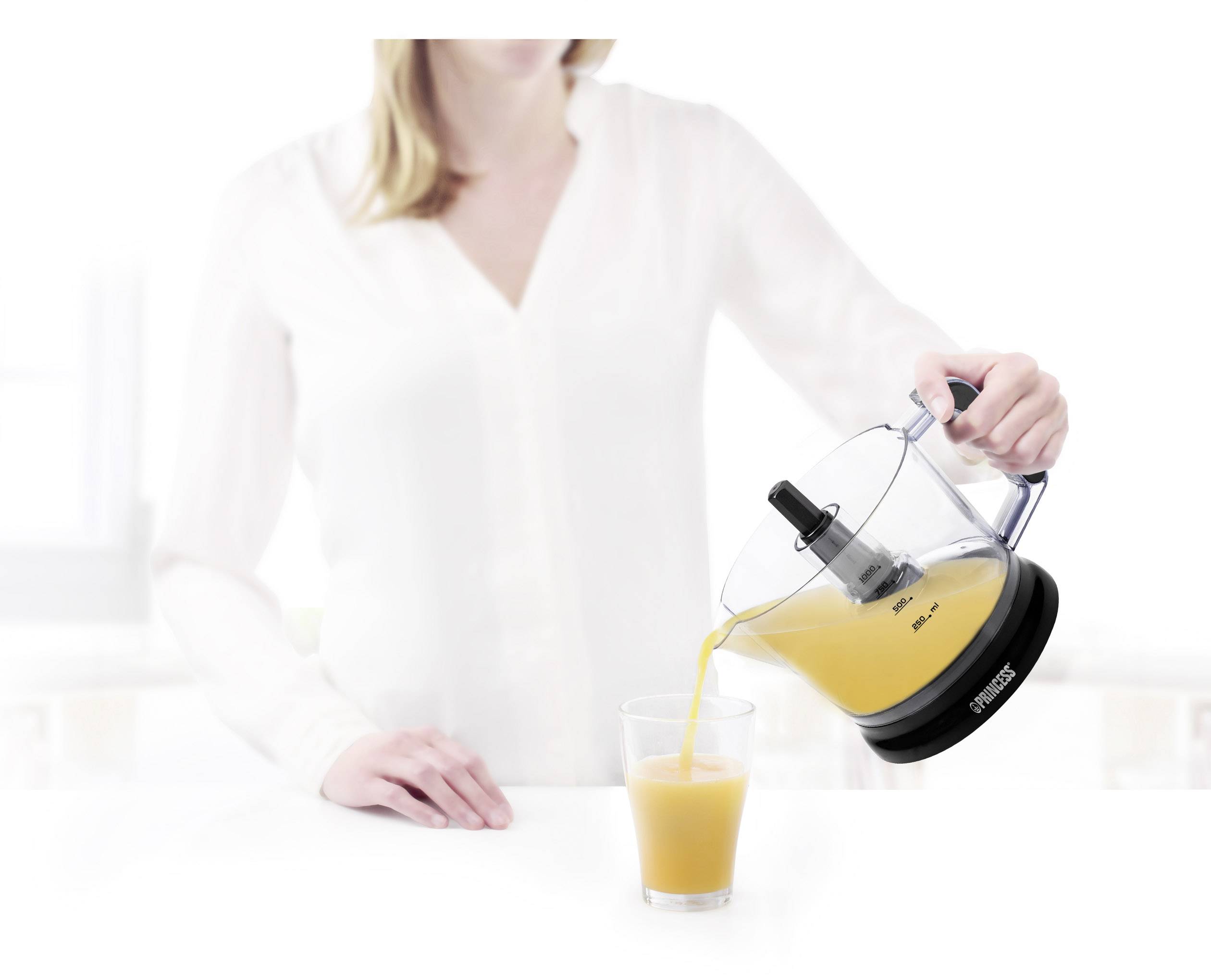 Een vrouw perst vers sinaasappelsap uit een elektrische sapcentrifuge in een glas. De sapcentrifuge staat op een lichte keuken.