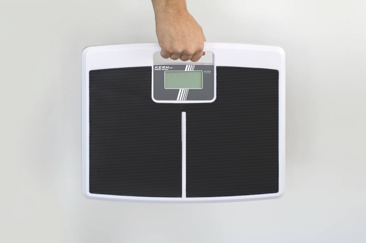 Een hand tilt een digitale personenweegschaal met een klein display in het midden.